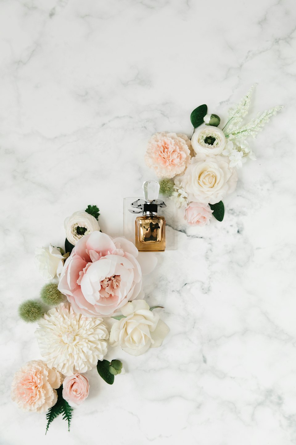 Gold perfume bottle with polka dot ribbon on marble with flowers.
