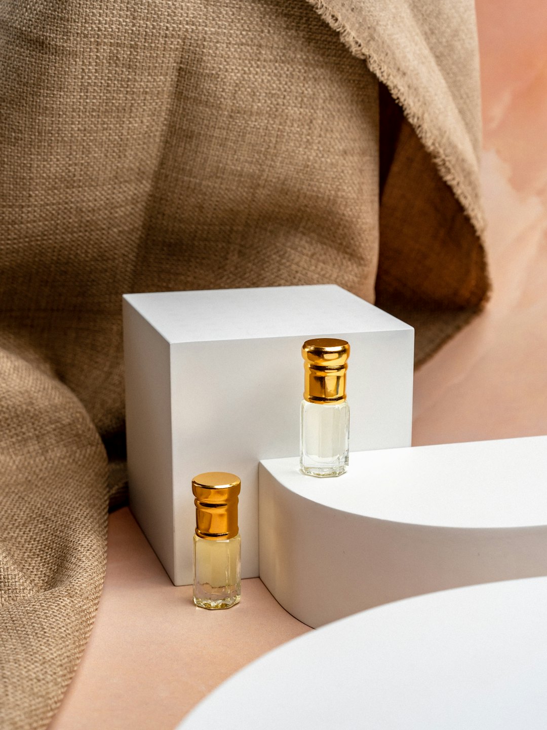 Two small glass perfume bottles with gold caps on white pedestals.